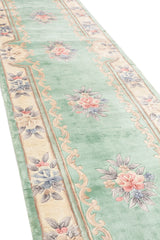 Vista lateral de la alfombra mostrando su textura suave y el diseño floral simétrico sobre fondo verde.