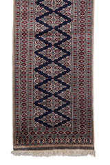 Detalle inferior de la alfombra persa que muestra los patrones romboidales entrelazados en azul marino y motivos florales en rojo y beige.