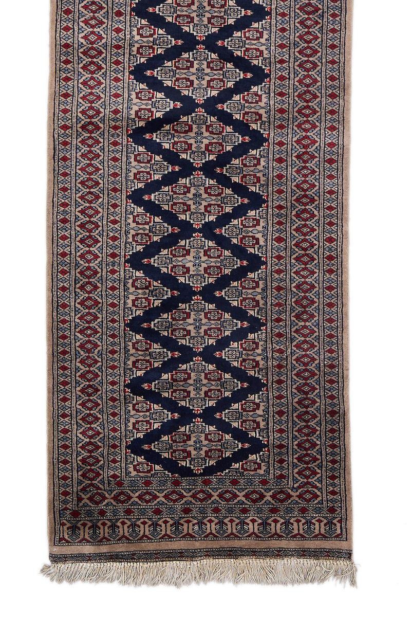 Detalle inferior de la alfombra persa que muestra los patrones romboidales entrelazados en azul marino y motivos florales en rojo y beige.