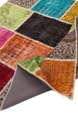 Imagen de la esquina levantada de la alfombra patchwork mostrando su reverso y el ensamblado artesanal de los retazos.