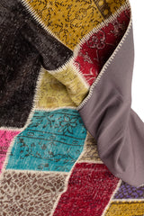 Imagen del reverso de la alfombra patchwork con la esquina doblada, revelando la base textil de color gris.