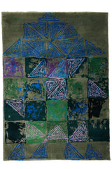 Vista completa de una alfombra moderna con base verde oliva, patrones triangulares azules y lilas, y bloques en tonos verdes, azules y morados.