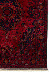 Detalle del borde inferior derecho de la alfombra mostrando motivos florales estilizados sobre fondo rojo y azul oscuro.