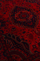 Primer plano del medallón central de la alfombra persa con intrincados detalles florales en rojo, azul oscuro y toques dorados.