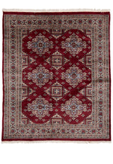 Vista frontal completa de una alfombra oriental de tonos burdeos con patrones geométricos repetitivos y guarda decorada en tonos beige y azul.