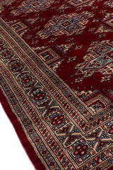 Toma en perspectiva de la alfombra que resalta su textura artesanal y los patrones intrincados sobre el fondo burdeos.