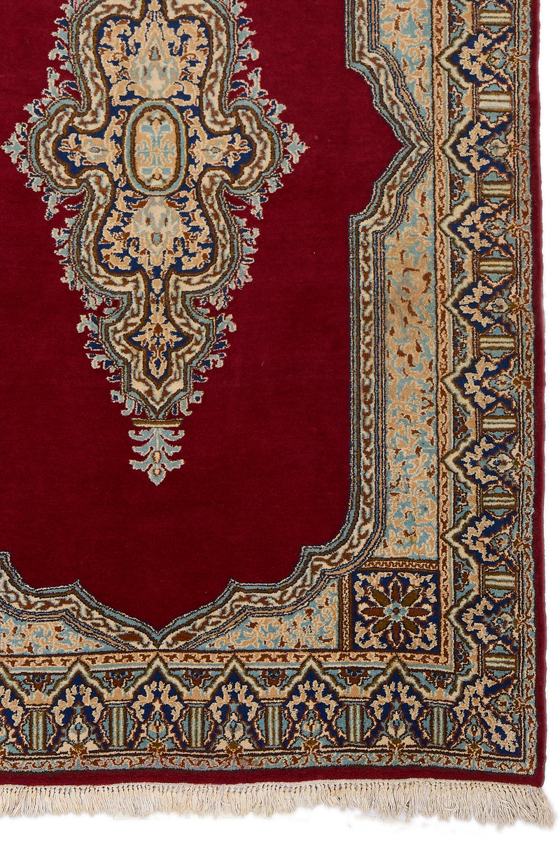 Detalle del extremo inferior derecho de la alfombra mostrando el diseño floral y geométrico en el borde azul y beige.