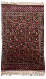 Vista completa de una alfombra oriental con diseño de cuadros geométricos en tonos burdeos, azul y ocre.