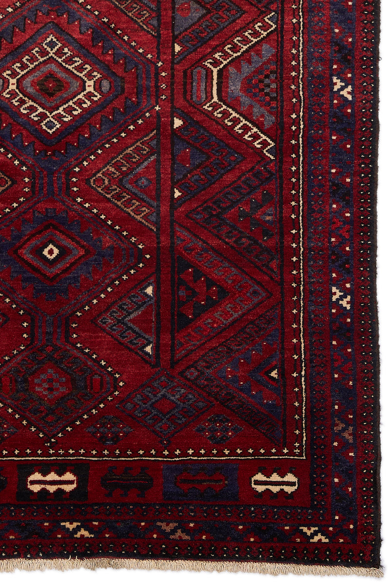 Detalle lateral inferior derecho de alfombra oriental con diseño geométrico rojo y azul sobre fondo burdeos