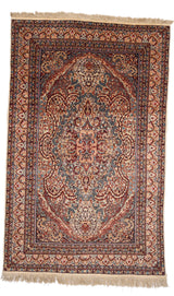 Vista superior completa de una alfombra persa con diseño central simétrico en tonos rojo, celeste, beige, rosado y detalles en negro.