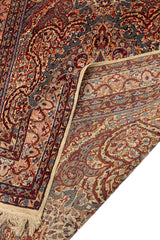 Vista del reverso de la alfombra con una esquina doblada, mostrando la precisión del tejido y los colores reflejados en el reverso: granate, celeste, beige y mostaza.