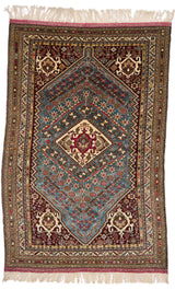 Vista completa de la alfombra oriental con fondo azul y detalles burdeos, beige y mostaza, destacando un medallón central geométrico con motivos florales.