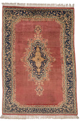 Alfombra persa con fondo terracota rojizo y medallón central azul marino con detalles en beige, borde decorado con motivos florales.
