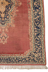 Detalle del borde de la alfombra con flores beige y rosa sobre fondo azul oscuro, sobre base terracota.