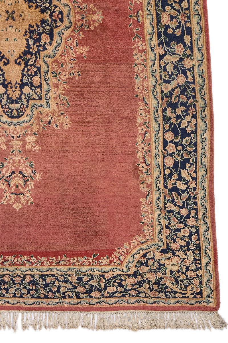 Detalle del borde de la alfombra con flores beige y rosa sobre fondo azul oscuro, sobre base terracota.