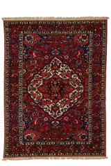 Vista frontal completa de alfombra persa con fondo rojo y medallón central floral en tonos marfil, rosa y negro.