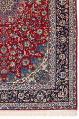 Detalle de la alfombra persa mostrando un diseño floral azul y beige sobre un fondo rojo.