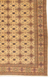 Detalle del borde de la alfombra mostrando los patrones florales y geométricos en tonos marrones y beige.