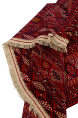 Vista cercana de la textura y el reverso de una alfombra oriental roja con detalles geométricos.