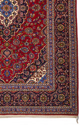 Detalle del borde de la alfombra mostrando patrones florales y geométricos en tonos azules y rojos.