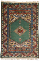 Alfombra oriental con fondo verde y detalles geométricos en el centro, borde decorado en tonos beige, rojo y azul.