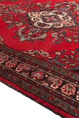 Vista en ángulo de alfombra persa roja mostrando su rica textura y borde oscuro.