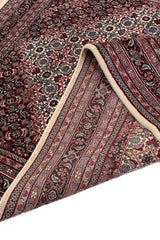Alfombra azul con diseño central de corona de flores y borde rojo decorado con motivos florales.