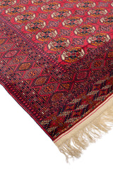 Primer plano del borde de una alfombra oriental roja mostrando los detalles de los patrones y la textura de los materiales.