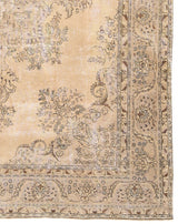Esquina de una alfombra beige con detalles ornamentales florales y bordes ligeramente desgastados.