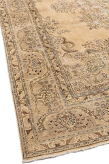 Vista en ángulo de una alfombra beige antigua con intrincados diseños florales en tonos desgastados.