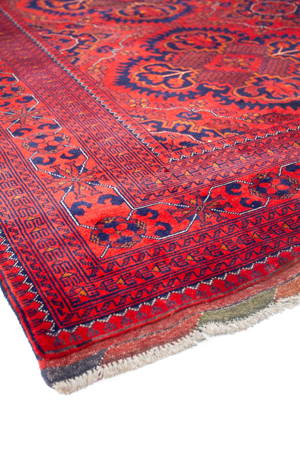 Detalle de esquina de alfombra roja con guarda decorativa y flecos en tono beige natural.