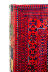 Primer plano del borde lateral de alfombra oriental roja con motivos geométricos en azul.