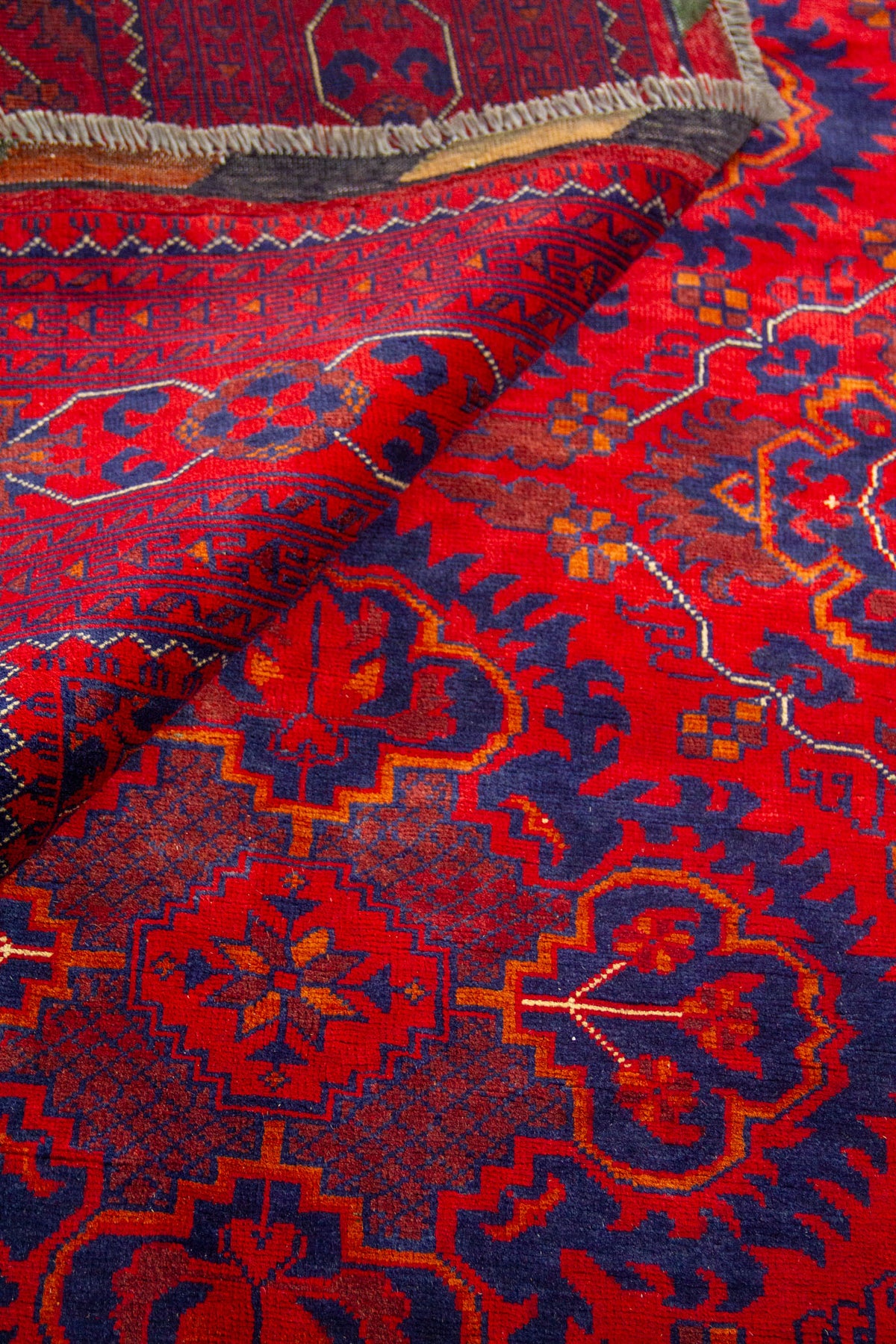 Alfombra oriental parcialmente doblada mostrando textura del tejido y definición de los motivos geométricos.