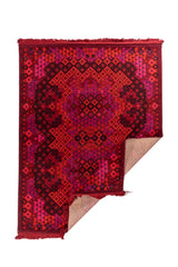 Alfombra artesanal de fondo rojo intenso con diseño geométrico tradicional y esquina doblada mostrando el reverso.