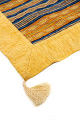 Detalle de esquina con borla en textil decorativo amarillo y azul con diseño de rayas