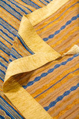 Detalle de textil Kayseri con rayas azules y amarillas, borde dorado y reverso visible