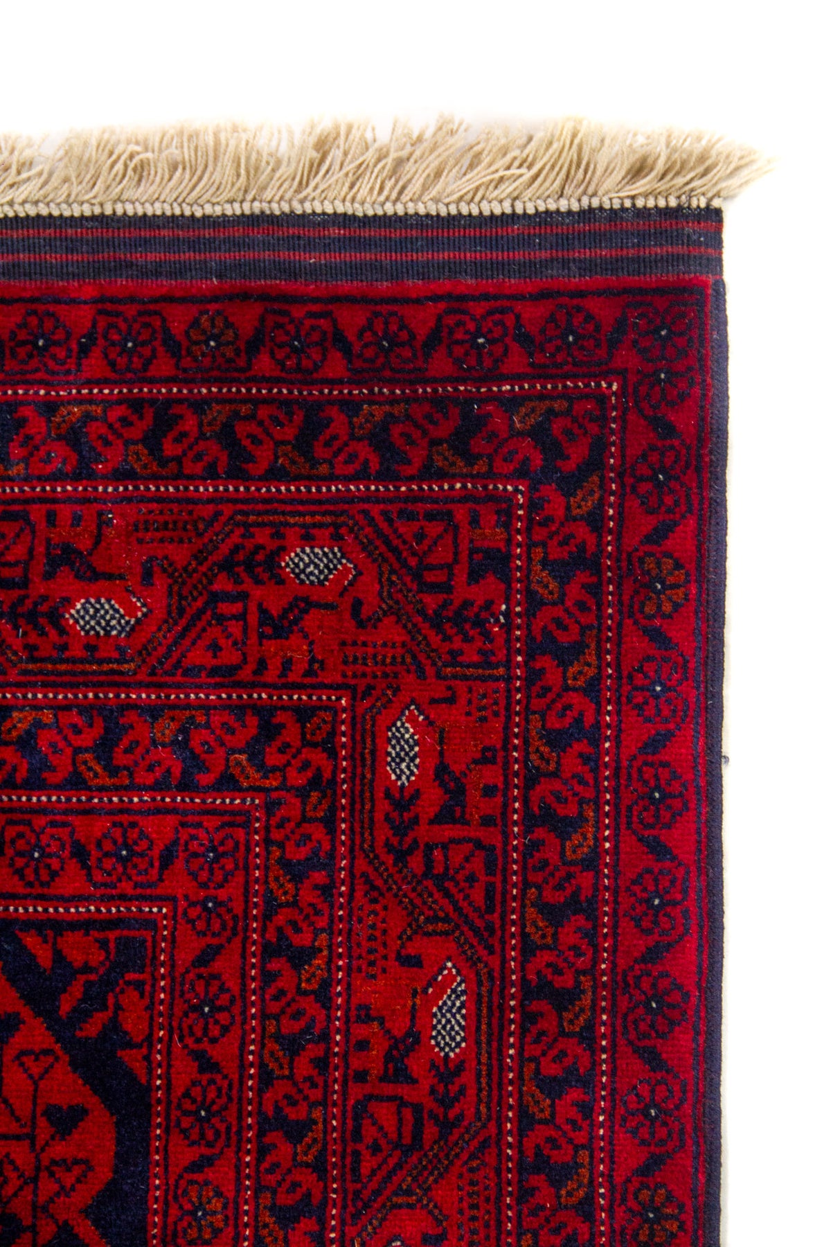Primer plano de la esquina superior de una alfombra roja con diseño artesanal, bordes ornamentales y flecos beige.