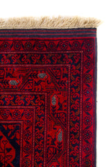 Primer plano de la esquina superior de una alfombra roja con diseño artesanal, bordes ornamentales y flecos beige.