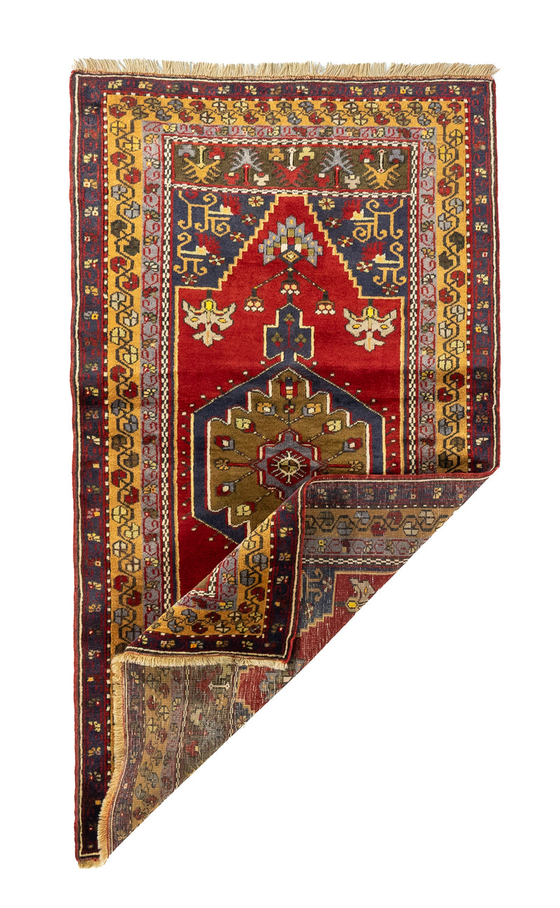 Alfombra roja de estilo oriental con una esquina doblada que muestra el reverso del tejido y sus detalles artesanales
