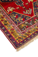 Detalle de esquina de alfombra roja con cenefa en azul oscuro, rojo y gris y motivos geométricos tradicionales