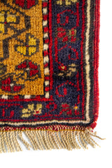 Detalle de alfombra doblada que muestra la textura del tejido, el reverso y las cenefas decorativas geométricas