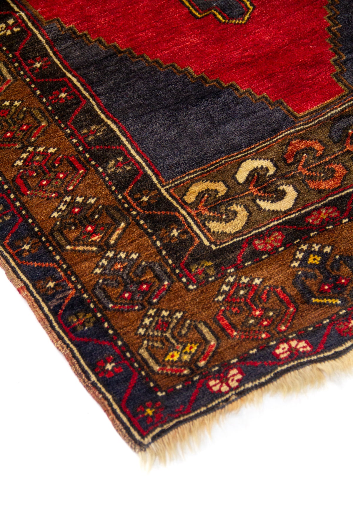 Detalle de esquina de alfombra oriental con borde geométrico en marrón, azul oscuro y rojo