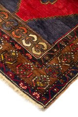 Primer plano de alfombra tradicional con campo rojo, fondo azul oscuro y cenefa geométrica artesanal