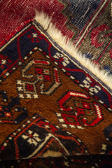 Detalle del borde de alfombra oriental con motivos geométricos pequeños en tonos marrón, rojo, azul y beige