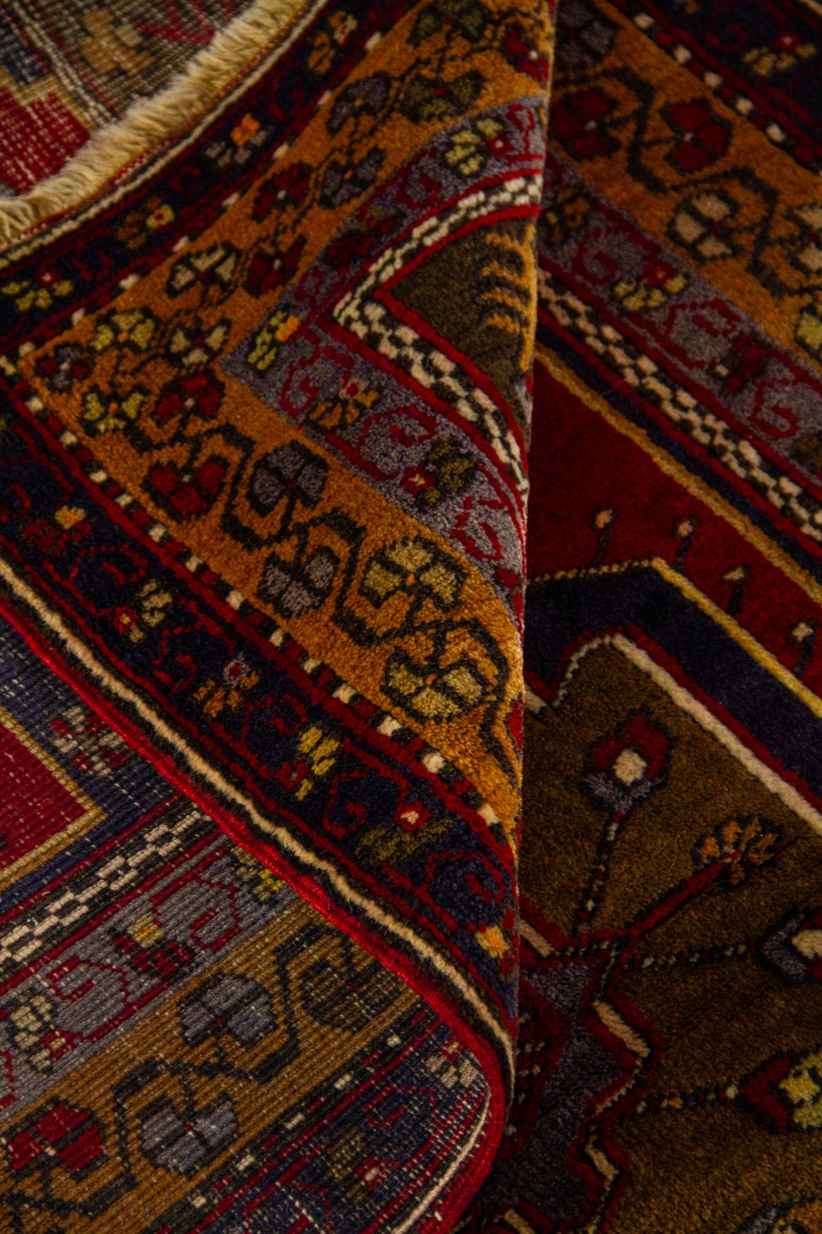 Detalle de alfombra doblada mostrando la textura del tejido, el reverso y la guarda geométrica multicolor