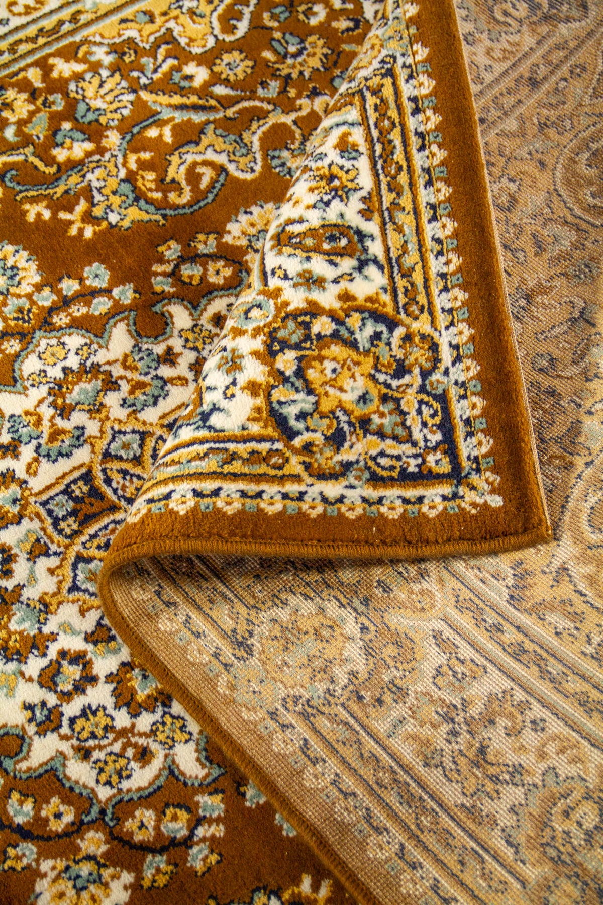 Detalle de alfombra oriental parcialmente doblada que deja ver el reverso, la textura del tejido y el diseño decorativo del borde.