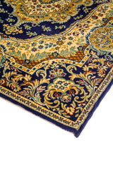 Detalle de esquina de alfombra azul marino con motivos florales y arabescos en tonos beige, dorado y celeste suave.