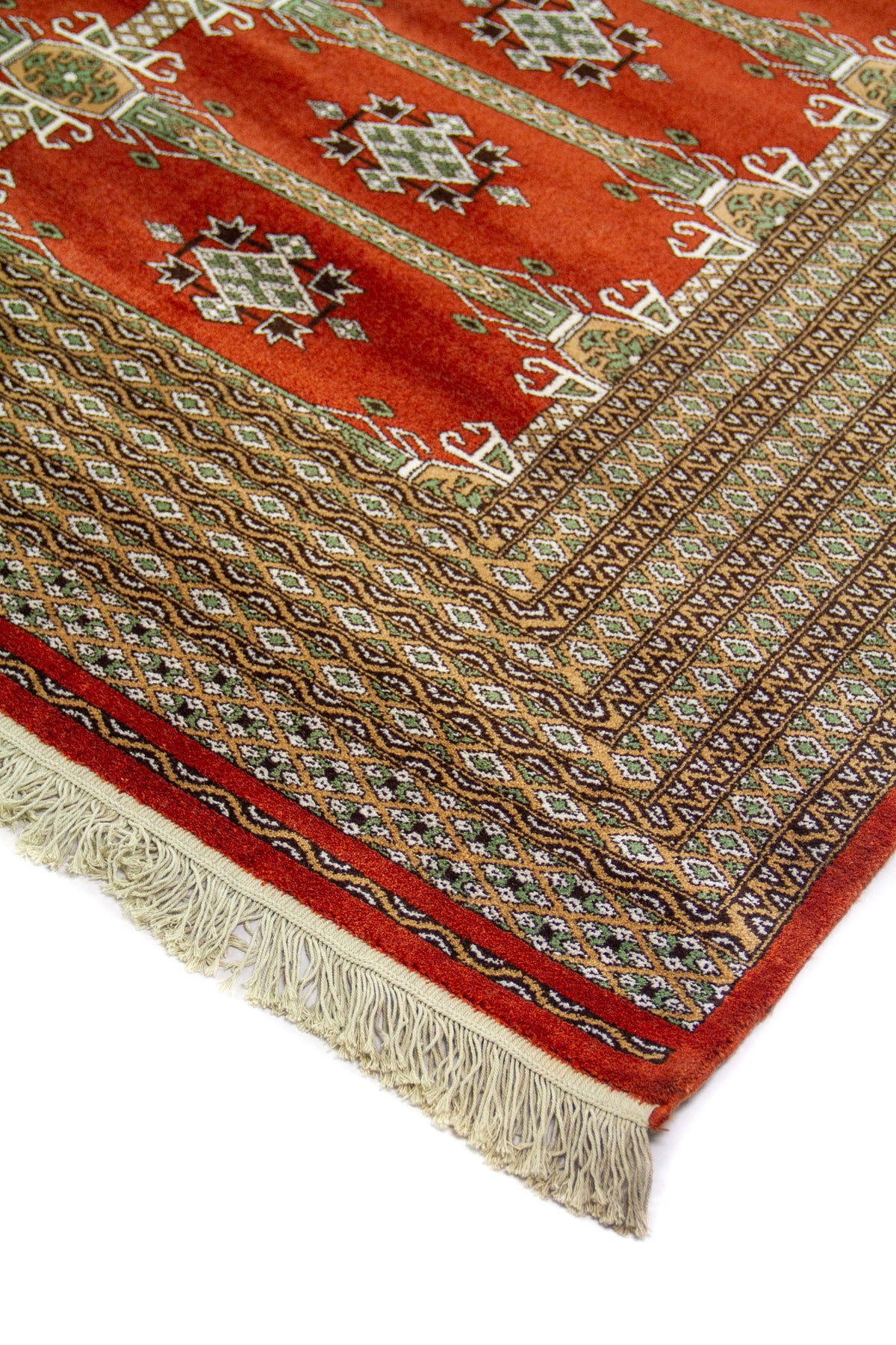 Detalle en perspectiva de esquina de alfombra oriental en tonos rojo y marrón, con guardas geométricas finas y flecos color blanco suave.