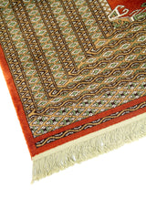 Primer plano de borde de alfombra geométrica con patrones repetitivos en beige, marrón y verde sobre fondo rojo.