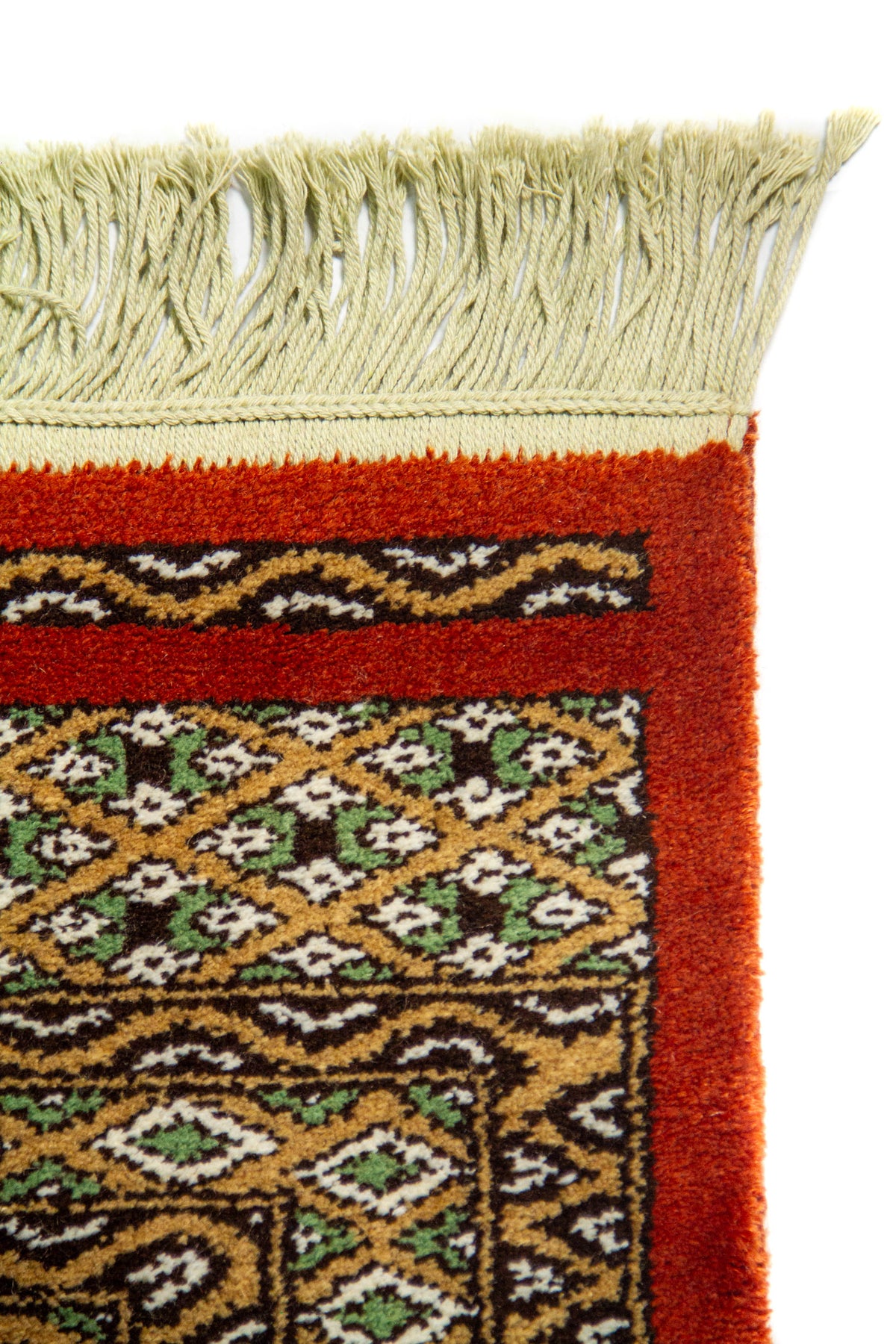 Detalle de esquina de alfombra con flecos claros, borde rojo liso y guardas geométricas 